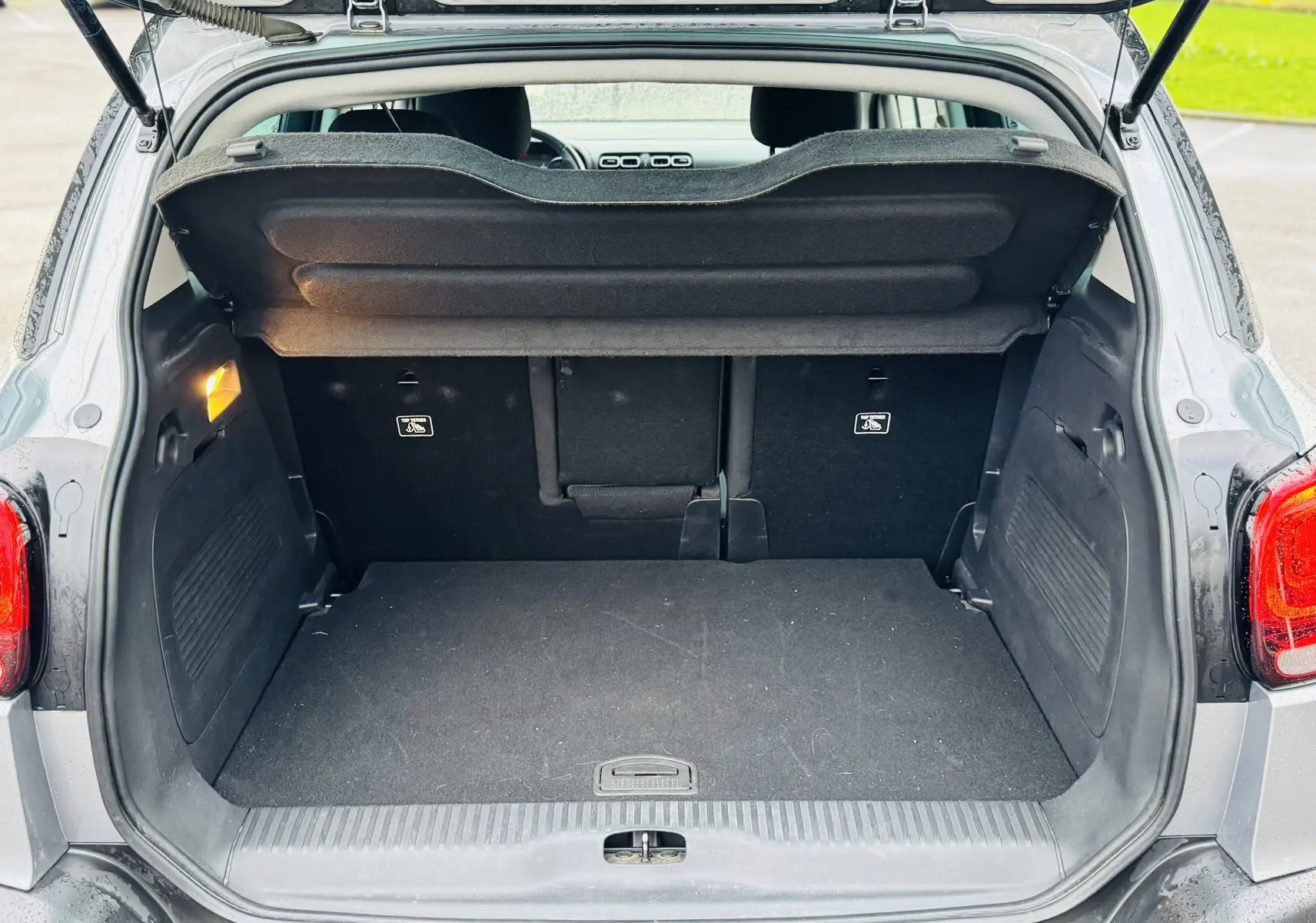 Coffre ouvert vu de l'arrière d'un Citroën C3 Aircross gris Artense avec banquette arrière et cache-bagages visibles.