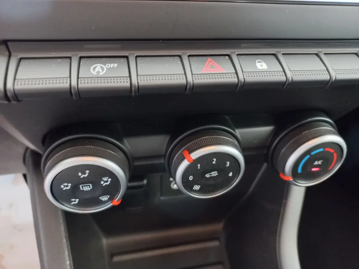 Gros plan sur les commandes de climatisation et boutons de fonction du tableau de bord noir de la Renault Clio Business blanche.