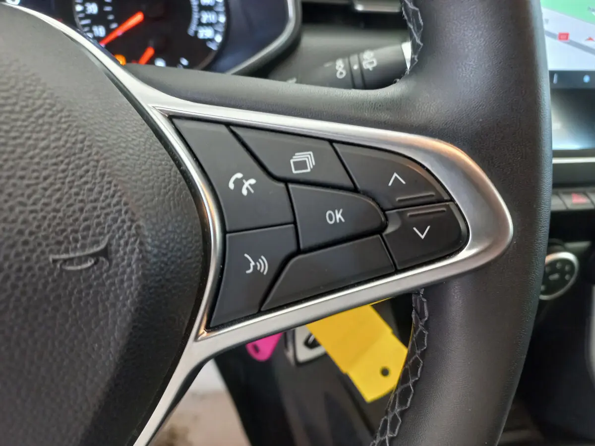 Gros plan sur les commandes multifonctions du volant cuir noir de la Renault Clio Business blanche de 2021.