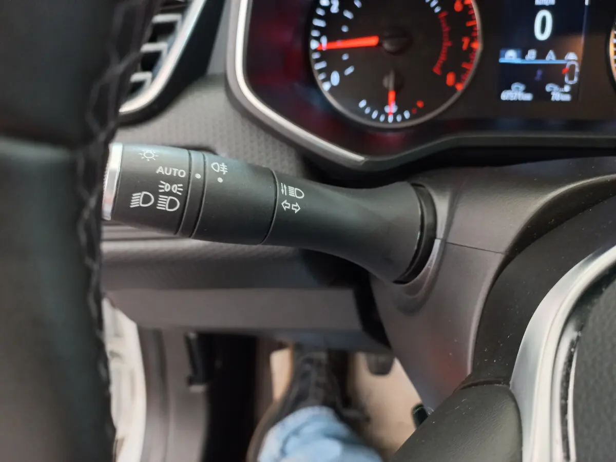 Gros plan sur la manette des feux à gauche du volant d'une Renault Clio Business blanche, tableau de bord partiellement visible.