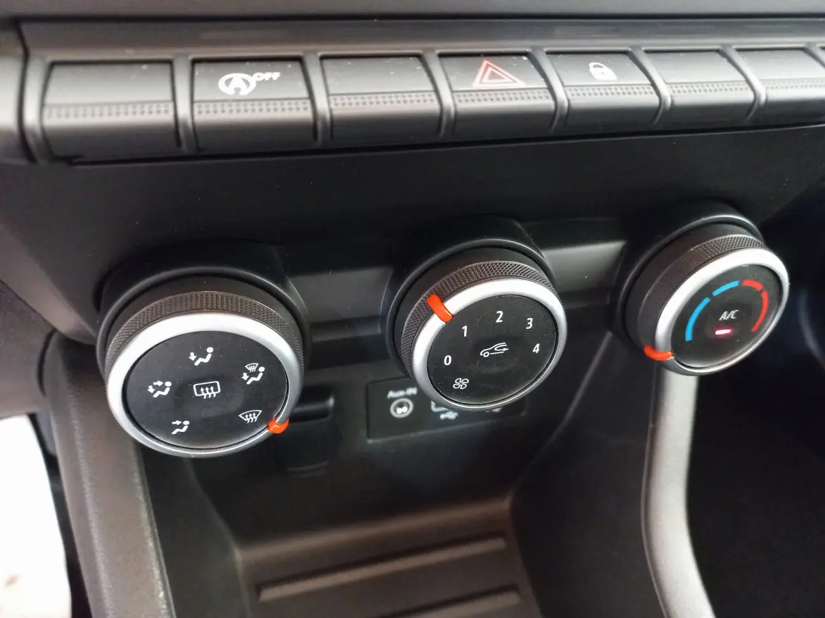 Gros plan sur les commandes de climatisation de la Renault Clio Business blanche, boutons noirs avec indicateurs rouges et bleus.