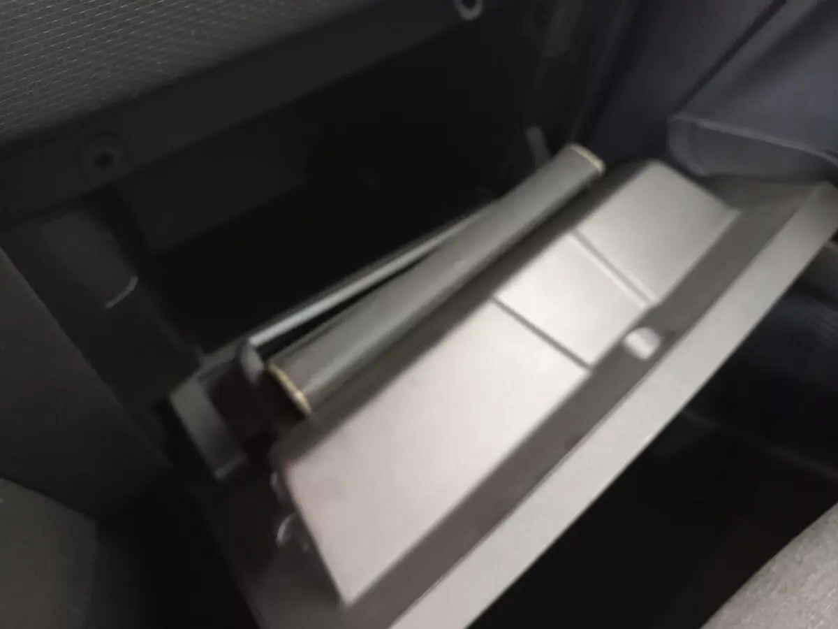 Gros plan sur la boîte à gants ouverte de la Renault Clio Business blanche, montrant l'intérieur sombre et le rangement.