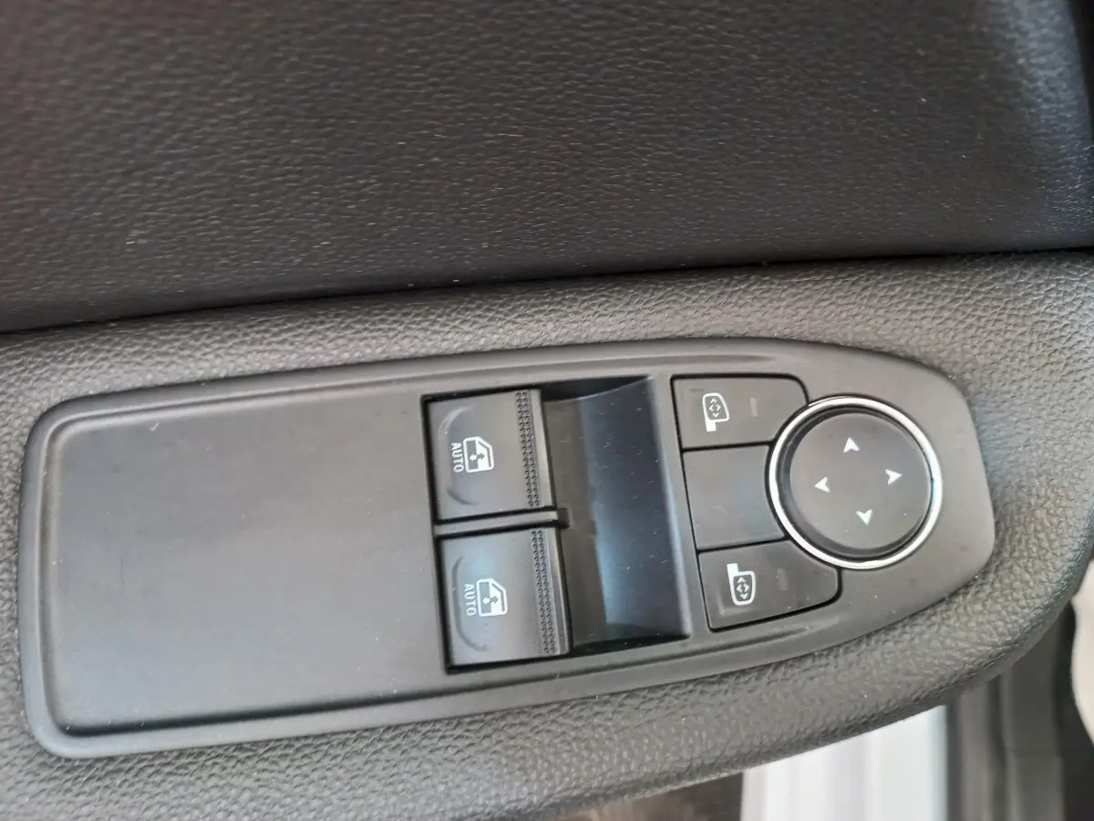 Gros plan sur les commandes de lève-vitres et réglage des rétroviseurs côté conducteur d'une Renault Clio blanche 2021.