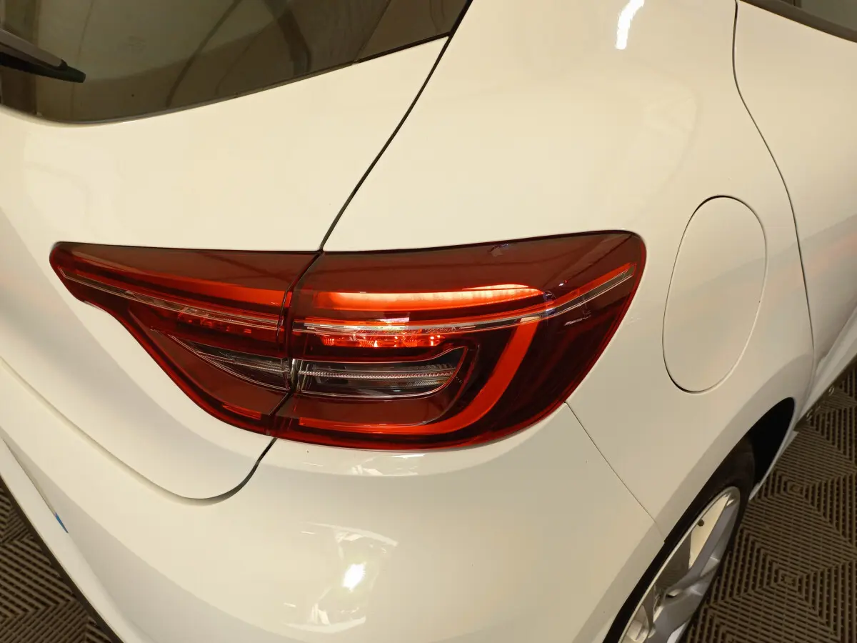 Gros plan sur le feu arrière droit rouge d'une Renault Clio blanche, avec la trappe à carburant visible sur le côté.