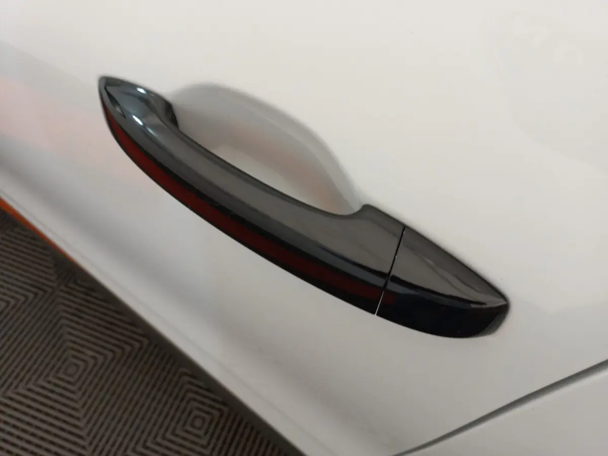 Poignée de porte noire en gros plan sur la portière blanche côté gauche d'une Renault Clio Business 2021.