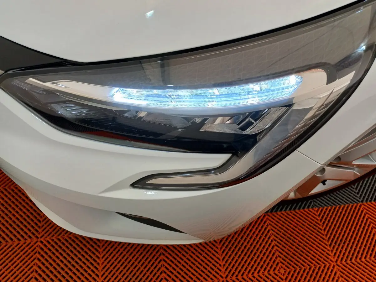 Gros plan sur le phare avant droit blanc d'une Renault Clio Business 2021, avec éclairage LED allumé sur sol orange.