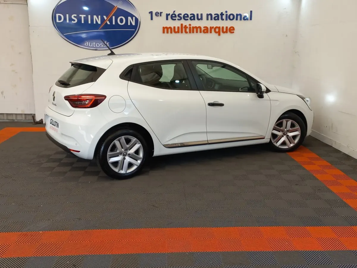 Profil droit d'une Renault Clio Business blanche 2021, avec jantes alliage et feux arrière LED visibles en intérieur showroom.