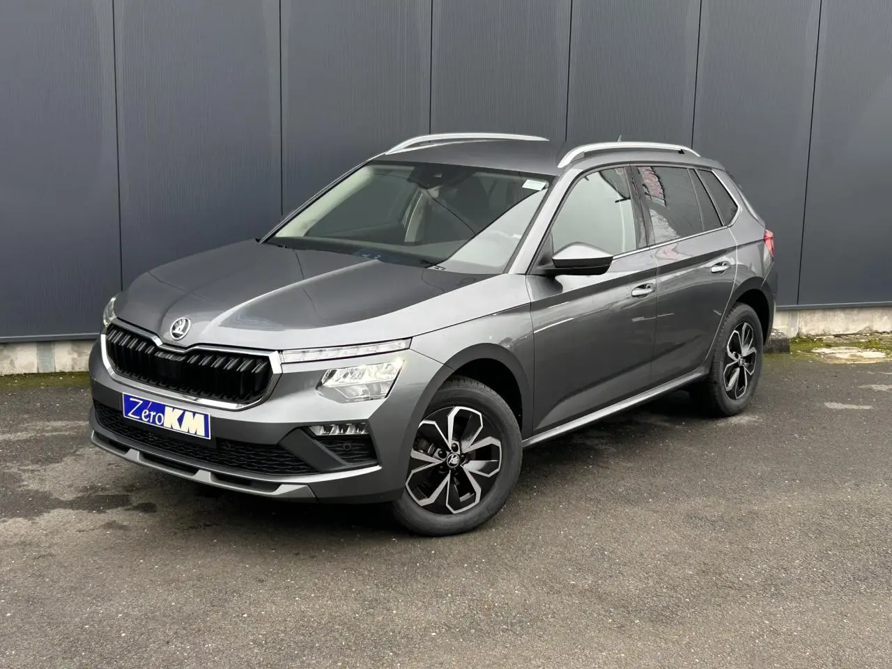 SUV Skoda Kamiq gris graphite vu en 3/4 avant droit, avec jantes alliage et barres de toit argentées.