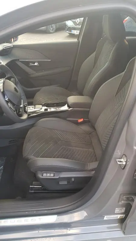 Vue intérieure côté conducteur de la Peugeot 208 Hybrid 110 e-DCS6 GT 2025 gris, sièges en tissu avec réglages électriques et volant réglable.