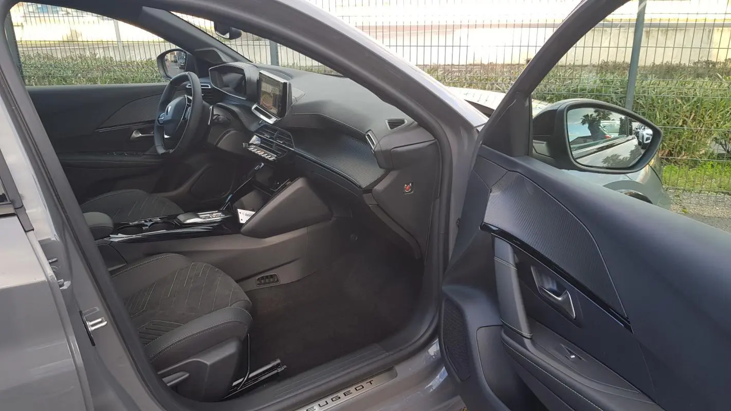 Vue intérieure côté conducteur de la Peugeot 208 Hybrid 110 e-DCS6 GT gris, avec tableau de bord et écran tactile visibles.