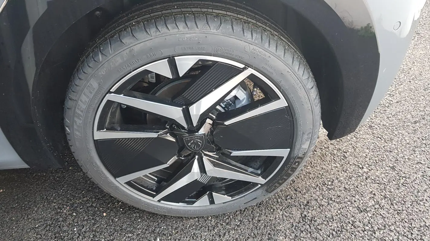 Gros plan sur la jante alliage 17 pouces noire et argentée du côté arrière droit d’une Peugeot 208 gris 2025.