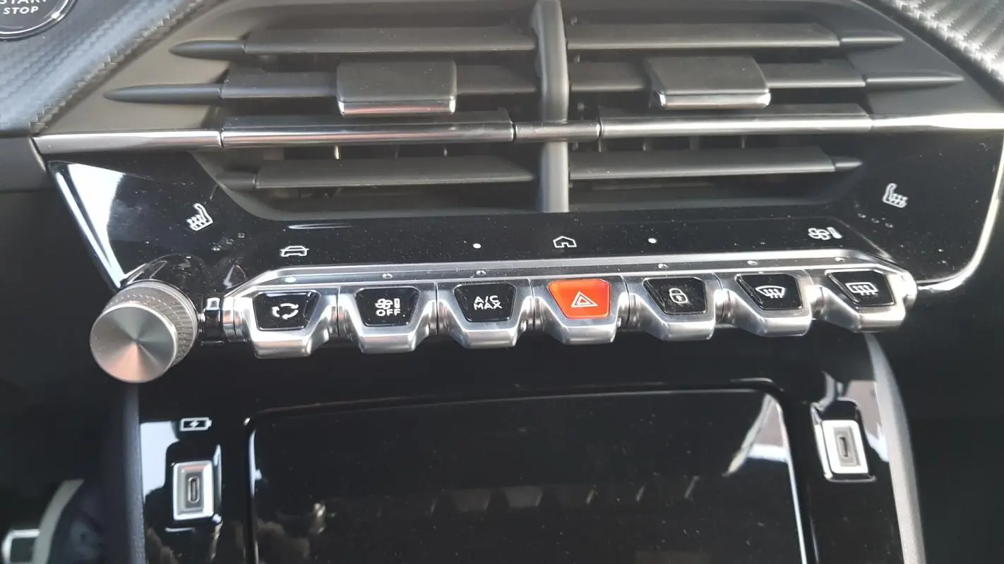 Vue rapprochée de la console centrale noire du Peugeot 208 Hybrid 110 e-DCS6 GT avec commandes clim et boutons chrome.