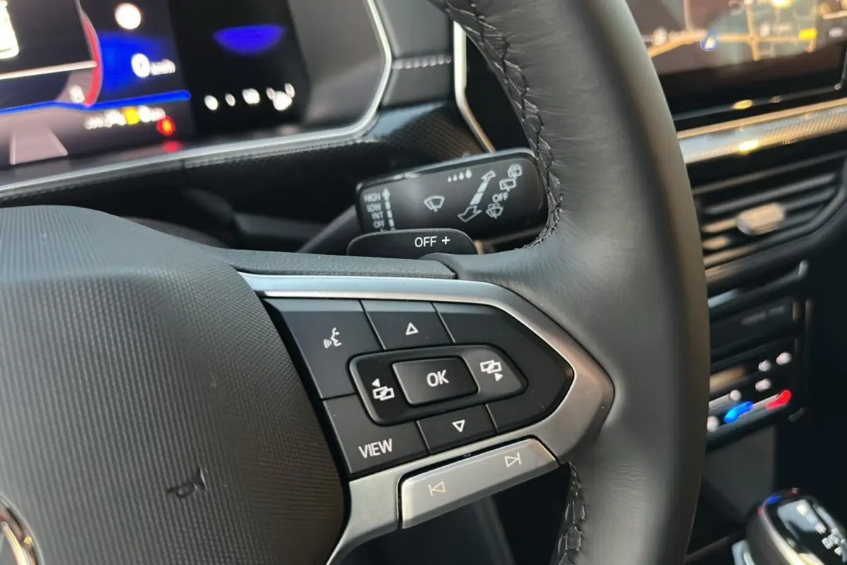 Gros plan sur le volant cuir multifonctions du Volkswagen T-Cross gris cendré, avec commandes et tableau de bord numérique en arrière-plan.