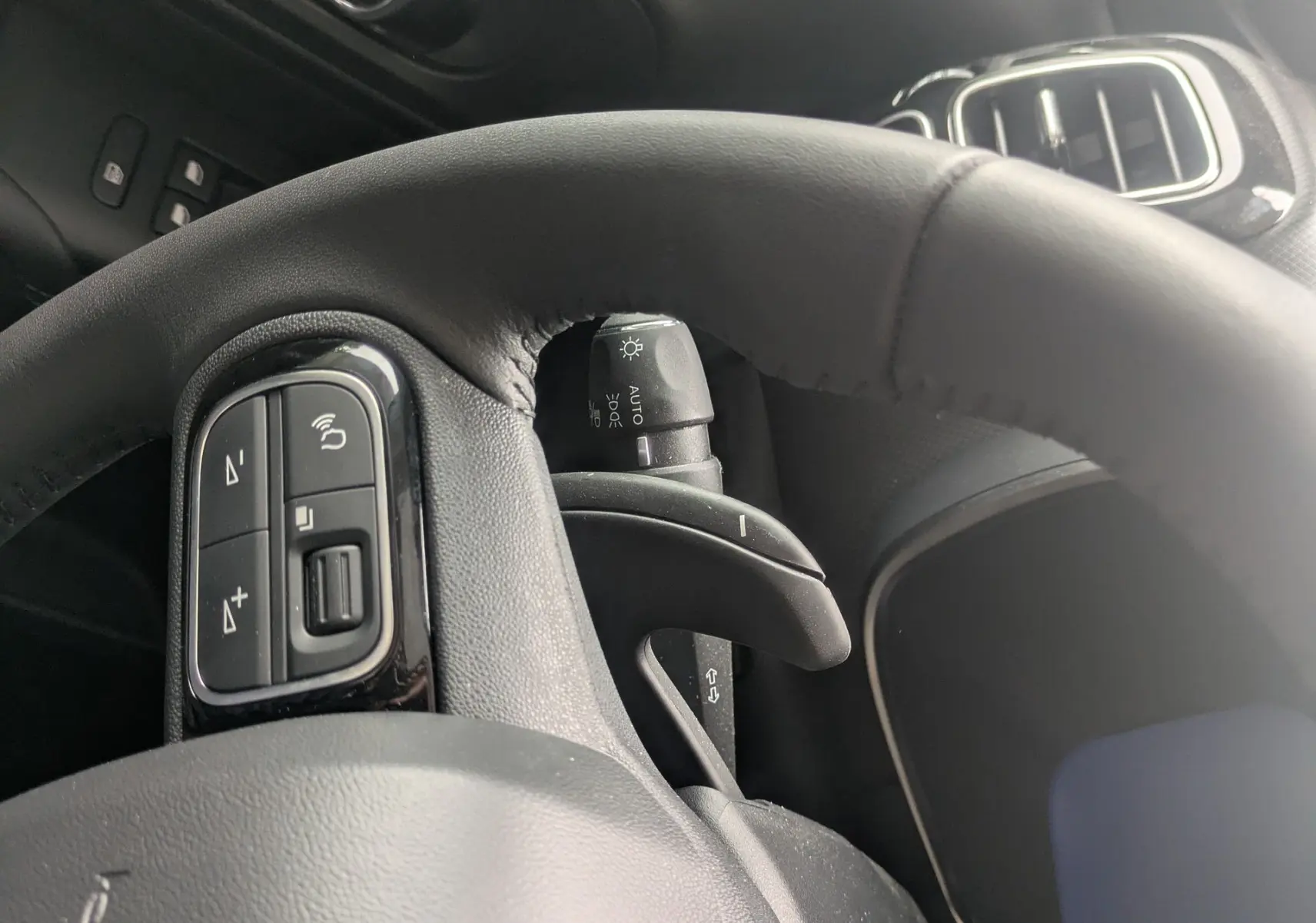 Vue rapprochée du volant en cuir et du tableau de bord noir du Citroën C5 Aircross hybride blanc, avec commandes au volant visibles.