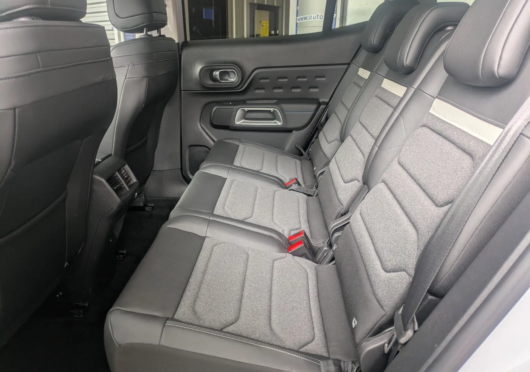 Vue intérieure côté droit sur la banquette arrière grise et noire du Citroën C5 Aircross Hybride 2025 avec porte et appuie-têtes visibles.