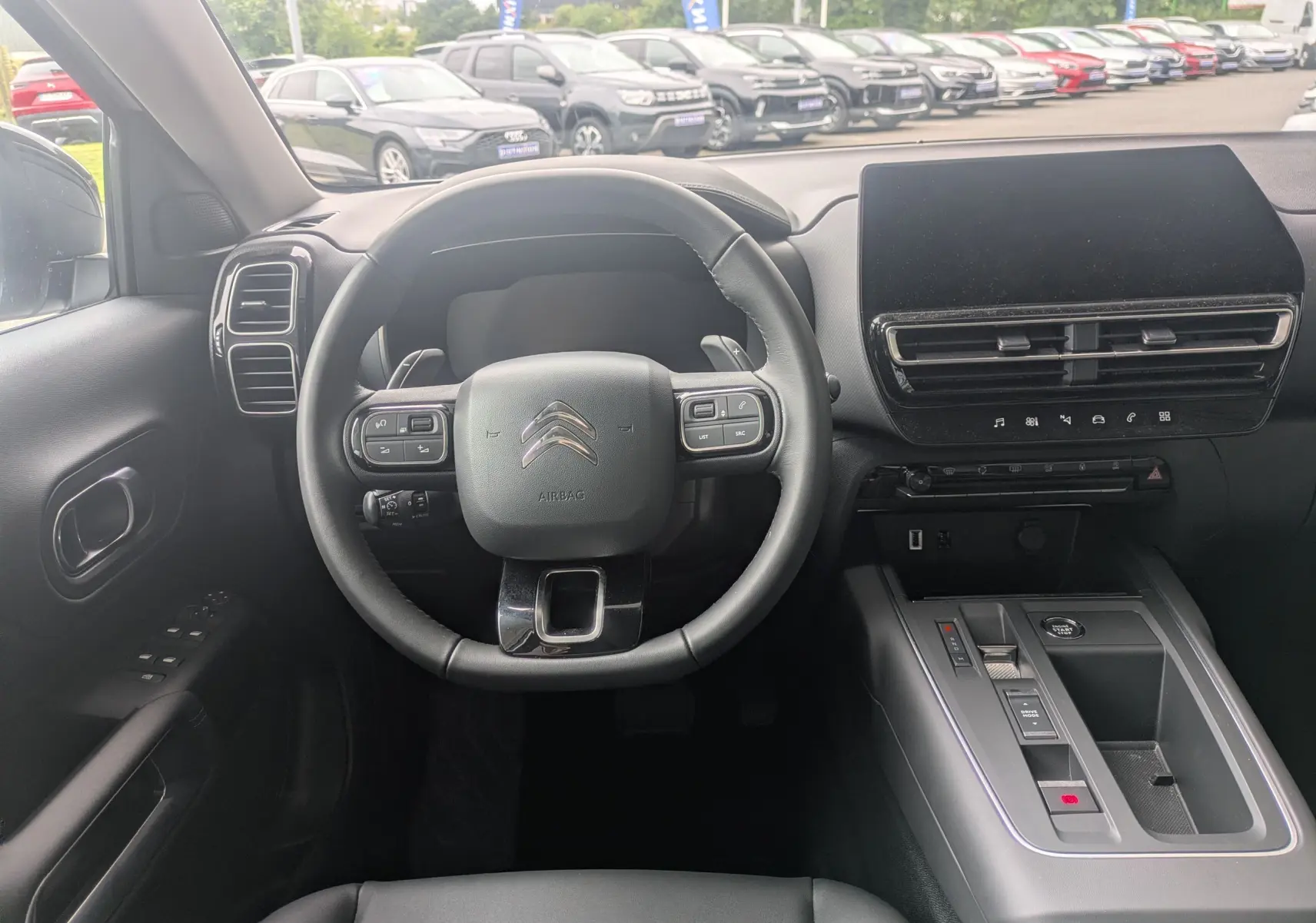 Vue intérieure centrée sur le volant et la console centrale du Citroën C5 Aircross hybride 2025, ambiance noire moderne.