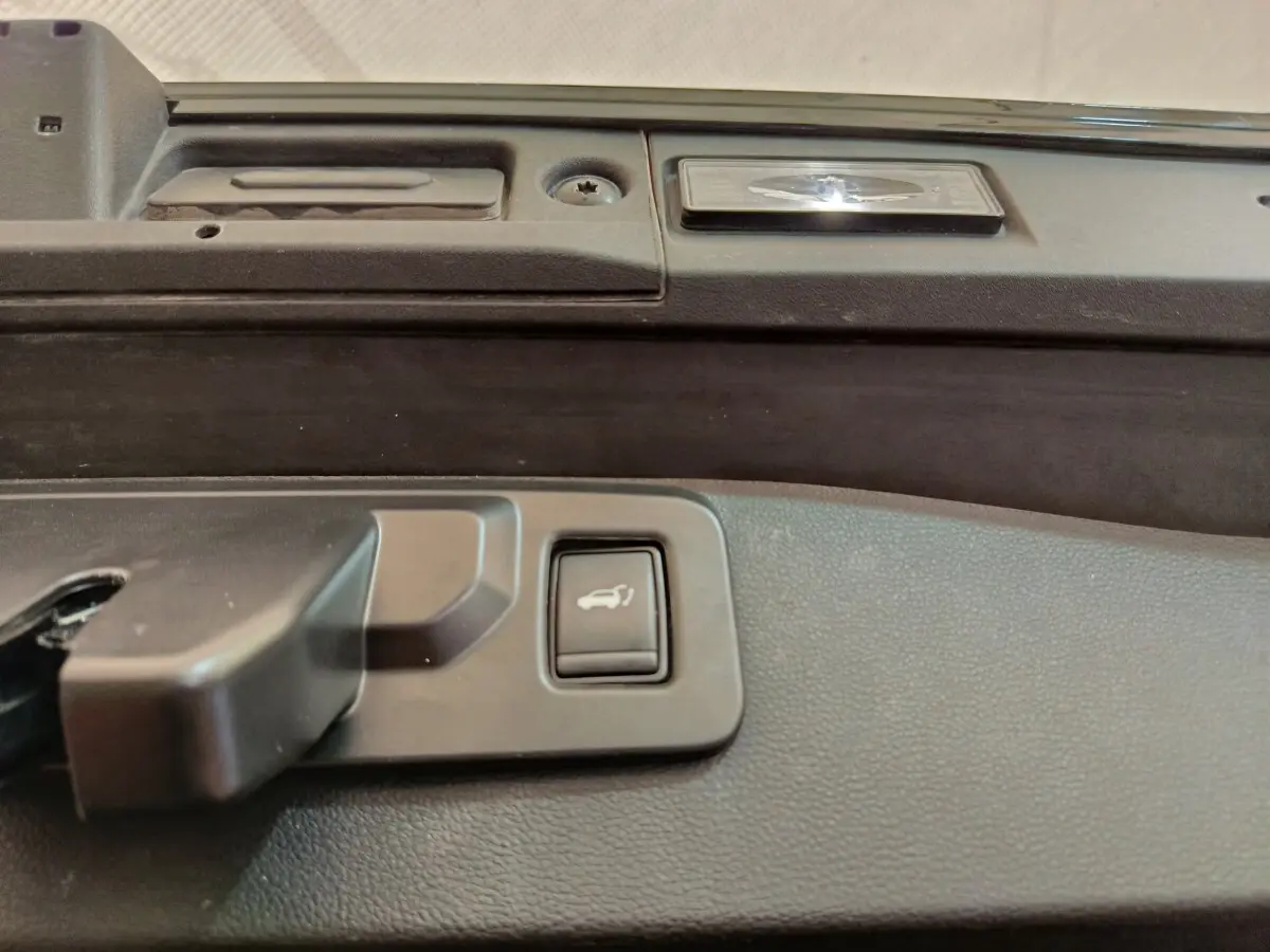 Bouton d'ouverture électrique du coffre sur la partie intérieure de la porte arrière du Renault Symbioz noir.
