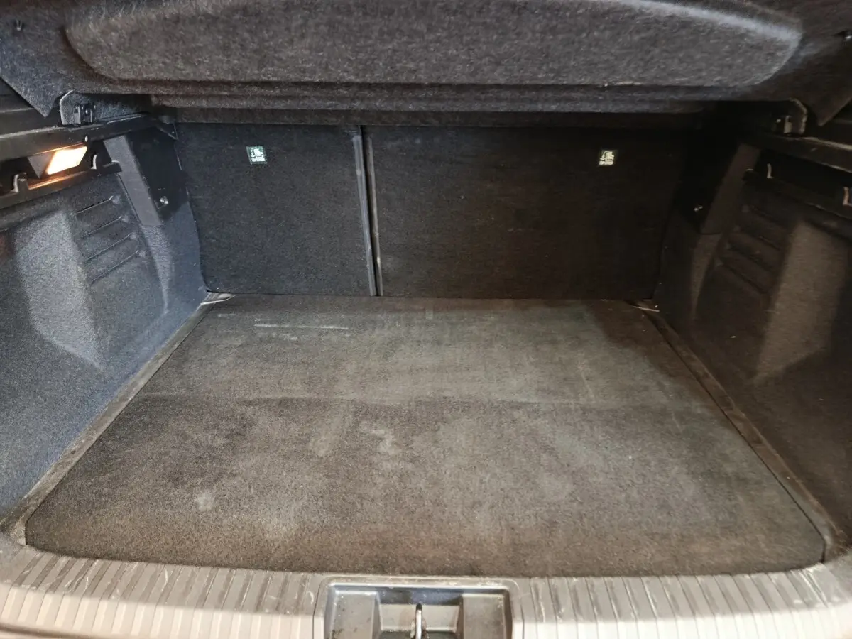 Coffre spacieux noir vu de l'intérieur, avec banquette arrière rabattue et éclairage latéral à gauche.