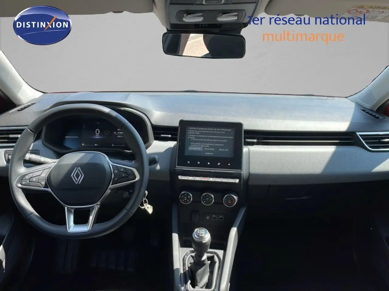Vue intérieure avant du tableau de bord et volant de la Renault Clio rouge flamme, avec écran tactile et boîte manuelle.