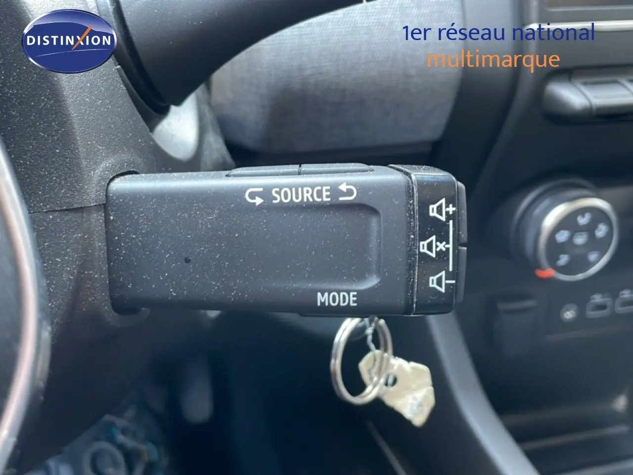 Gros plan sur la commande au volant gauche de la Renault Clio rouge flamme, avec bouton source et mode visible.