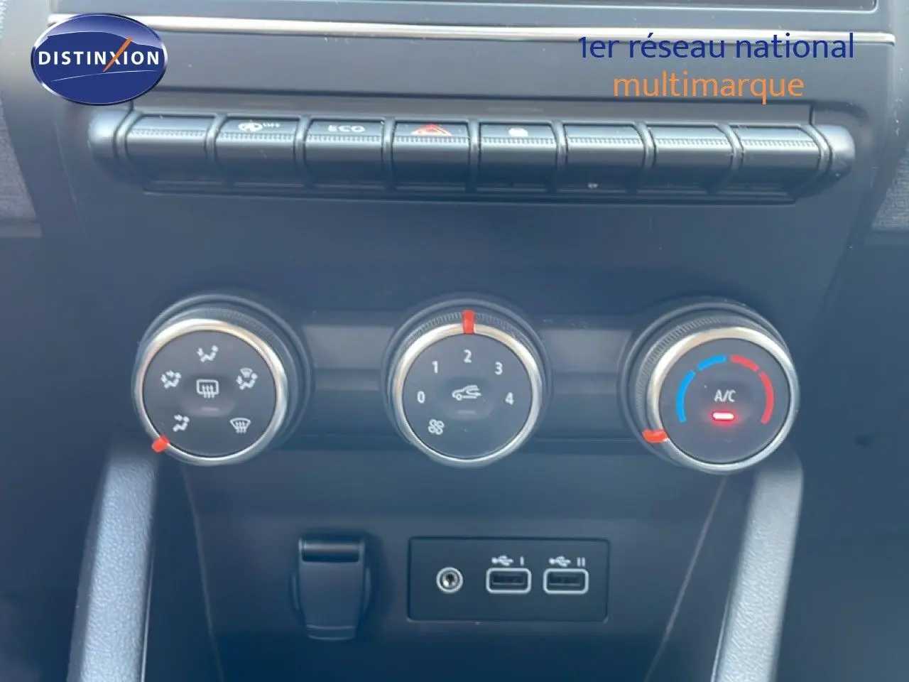 Gros plan sur les commandes de climatisation et les ports USB du tableau de bord d’une Renault Clio rouge flamme 2025.