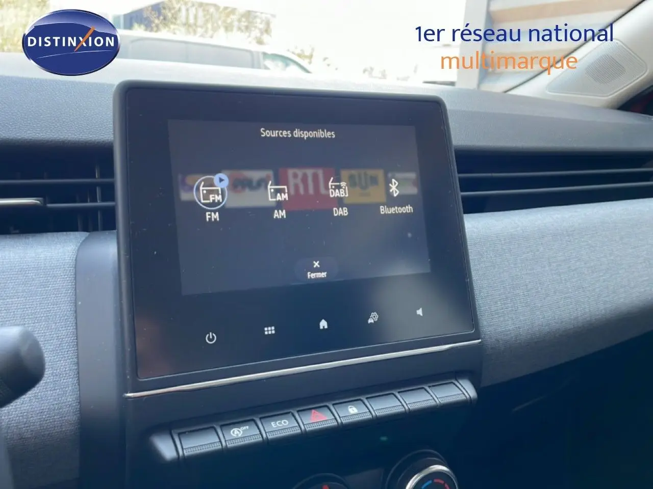 Écran tactile central affichant les sources audio dans l’habitacle d’une Renault Clio rouge flamme métal, vue de face.