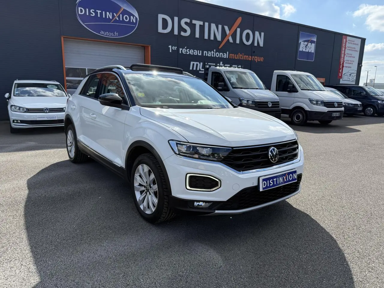 Volkswagen T-Roc blanc en 3/4 avant droit, avec toit ouvrant en verre et calandre noire distinctive.
