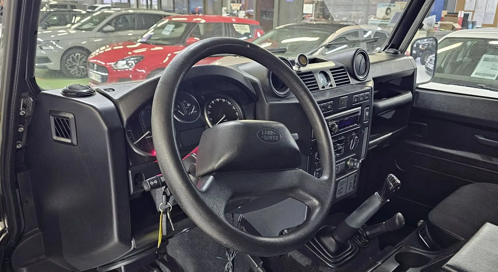 Vue intérieure côté conducteur du Land Rover Defender 110 Station Wagon gris de 2010, volant et tableau de bord visibles.