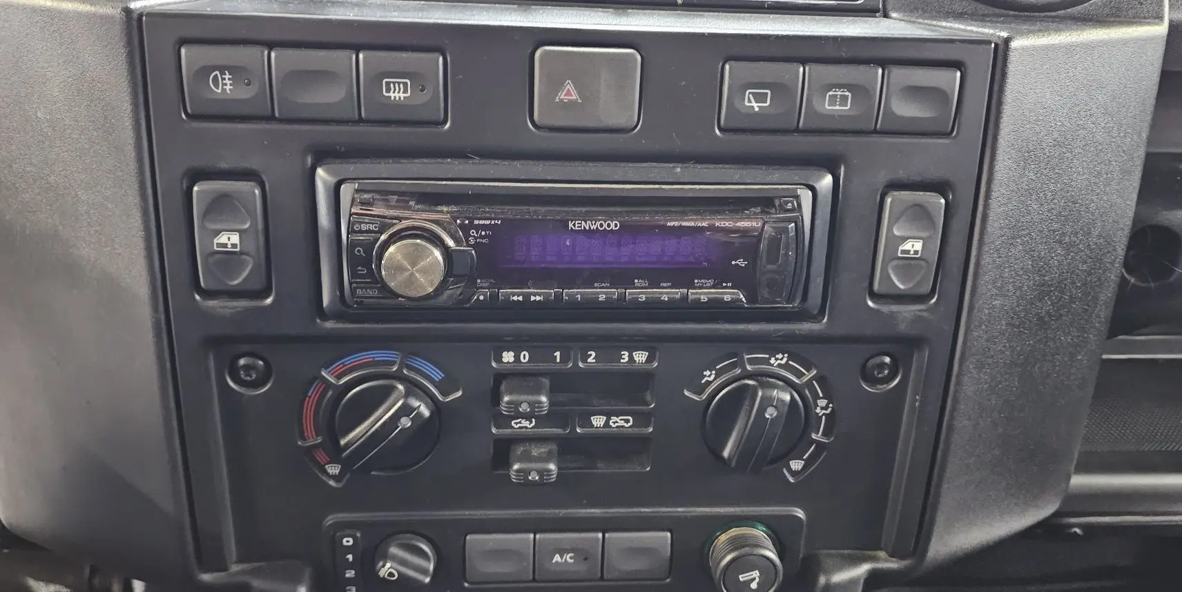 Tableau de bord du Land Rover Defender 110 II Station Wagon gris, montrant la radio Kenwood et les commandes de climatisation.
