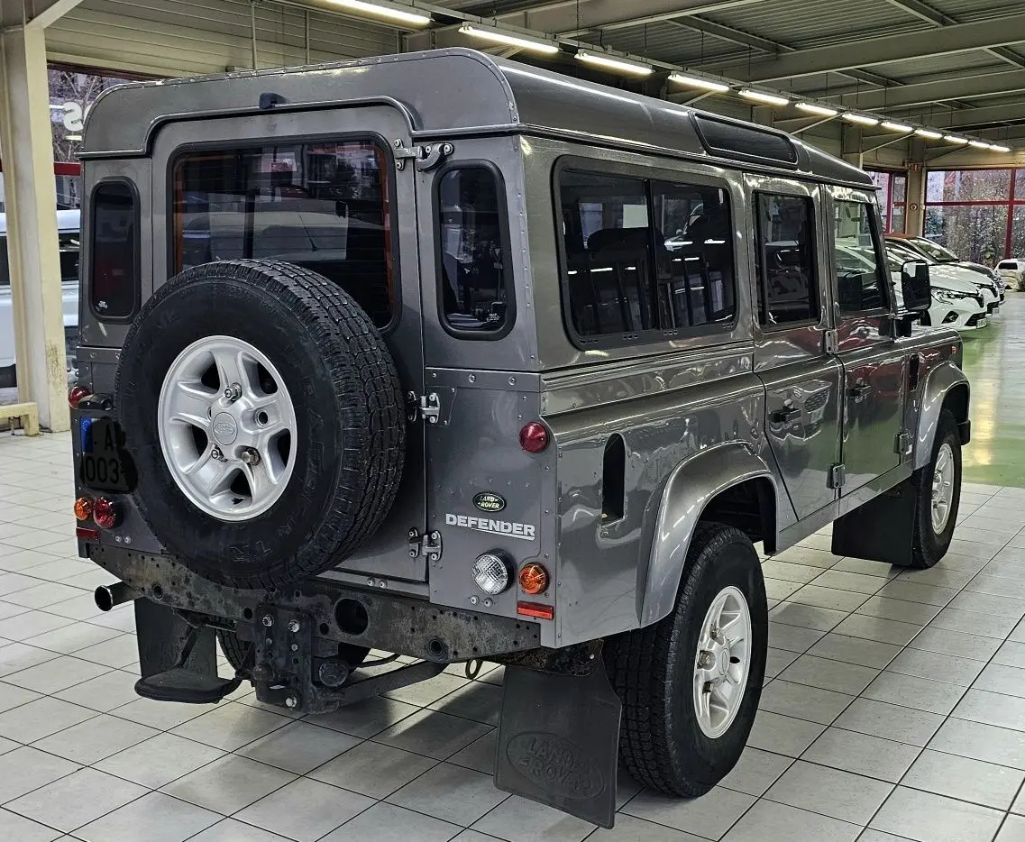 Vue 3/4 arrière droite d'un Land Rover Defender 110 Station Wagon S gris, avec roue de secours fixée à la porte arrière.