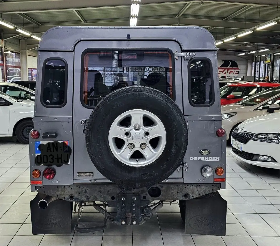 Vue arrière d'un Land Rover Defender 110 Station Wagon gris, avec roue de secours fixée sur la porte arrière.