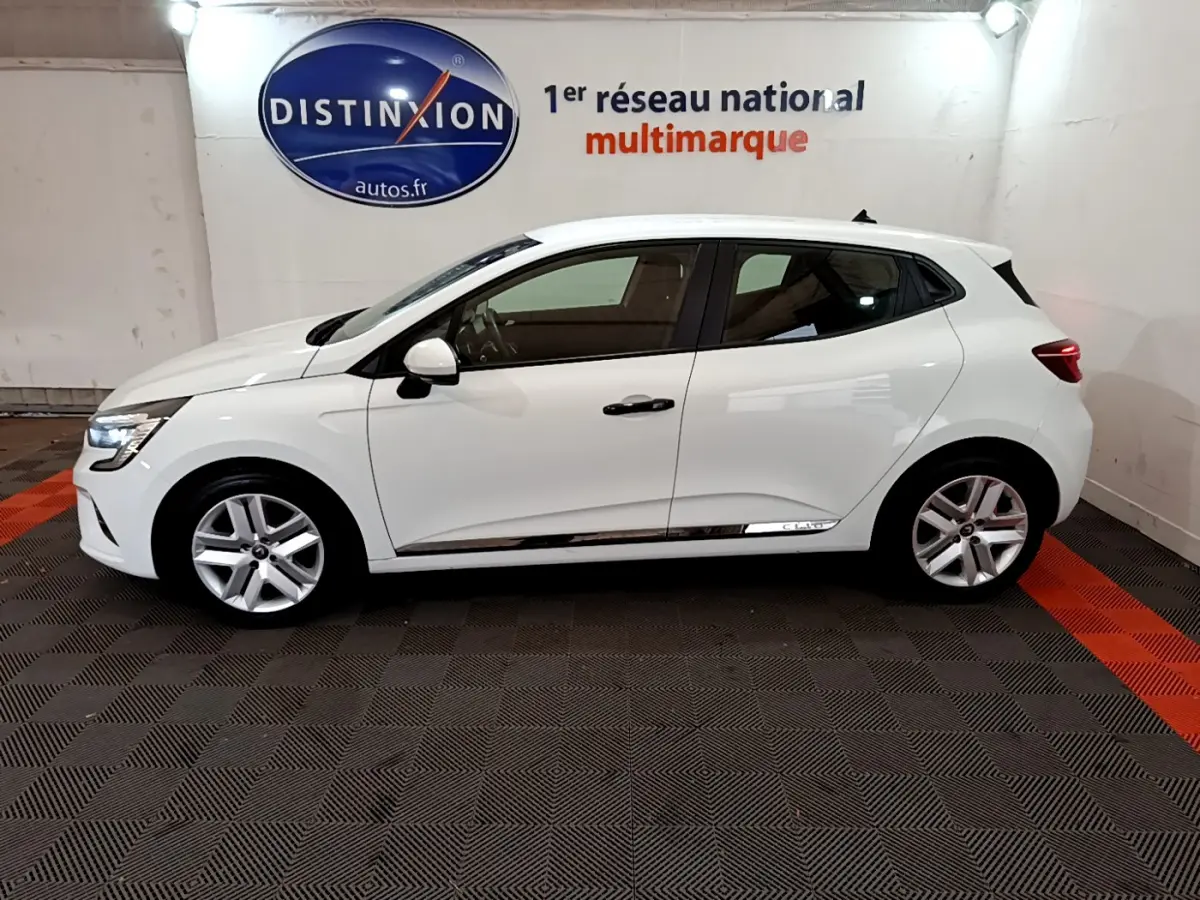 Profil droit d'une Renault Clio Business blanche 2021, avec jantes alliage et feux arrière LED visibles en intérieur showroom.