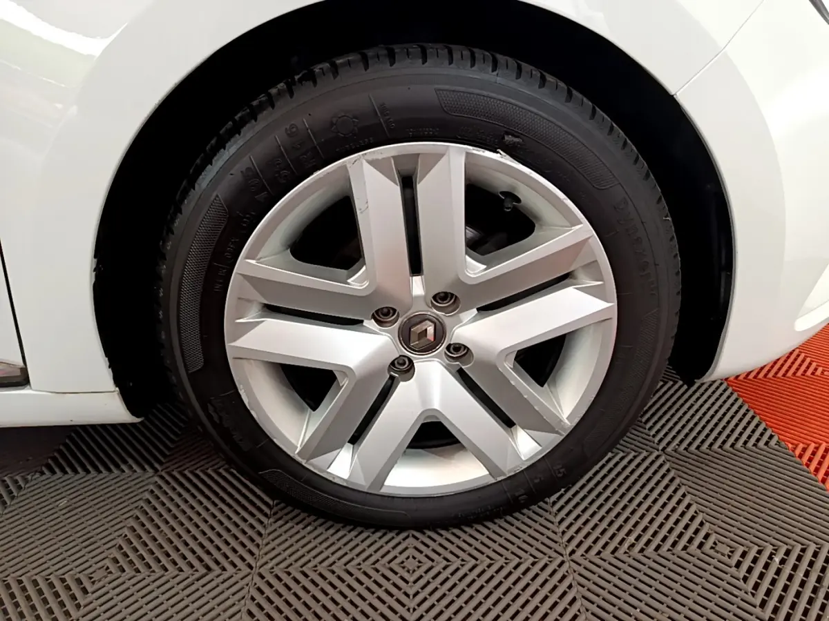 Gros plan sur la roue avant gauche d'une Renault Clio blanche, jante alliage au design moderne.