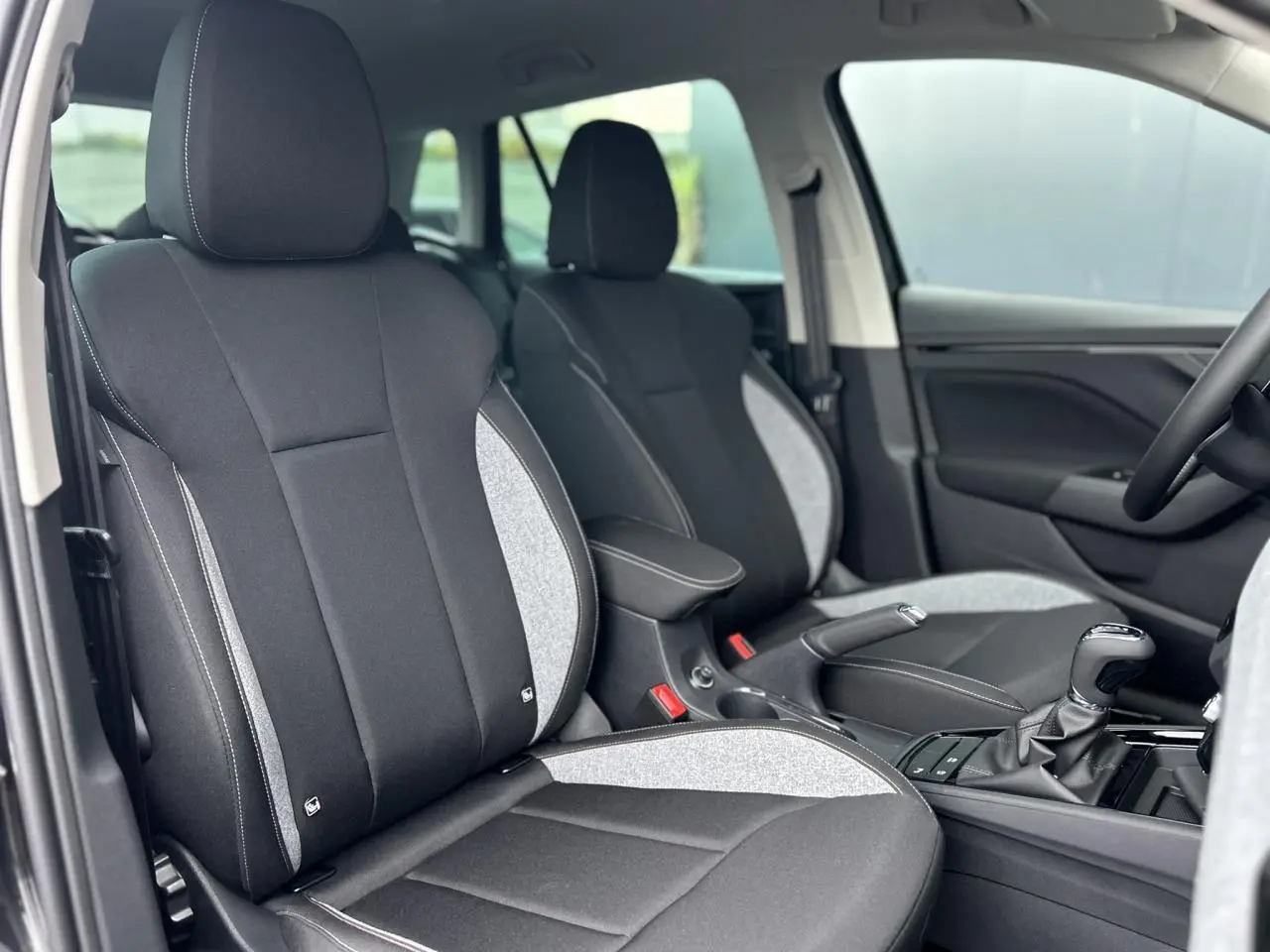 Vue intérieure côté conducteur du Skoda Kamiq 2025 noir Magic, sièges bi-matière noirs et gris avec surpiqûres blanches.