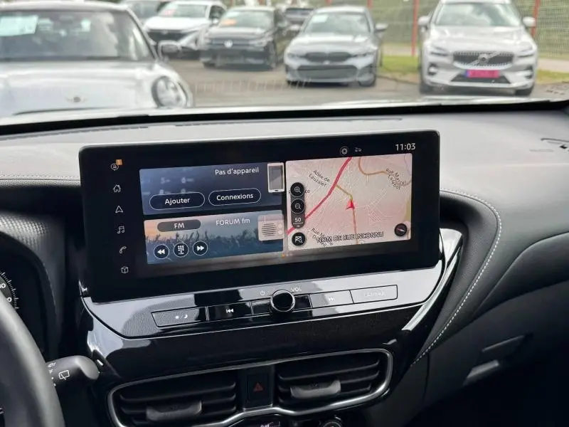 Vue intérieure du tableau de bord du Nissan Juke 2025 avec écran tactile multifonction affichant navigation et radio.