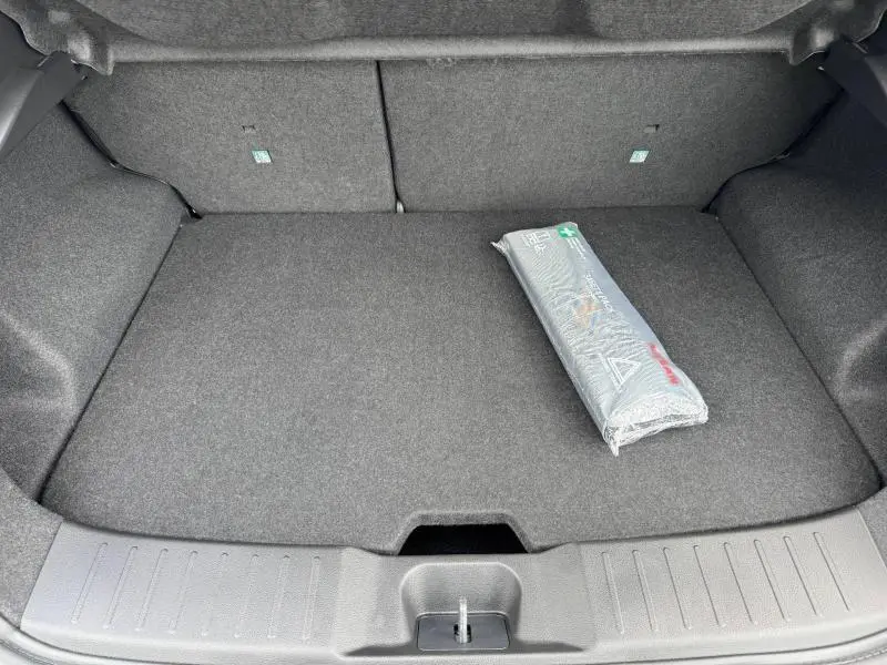 Coffre ouvert vu de face d'un Nissan Juke 2025 noir Kuro, avec tapis gris et trousse de secours emballée.
