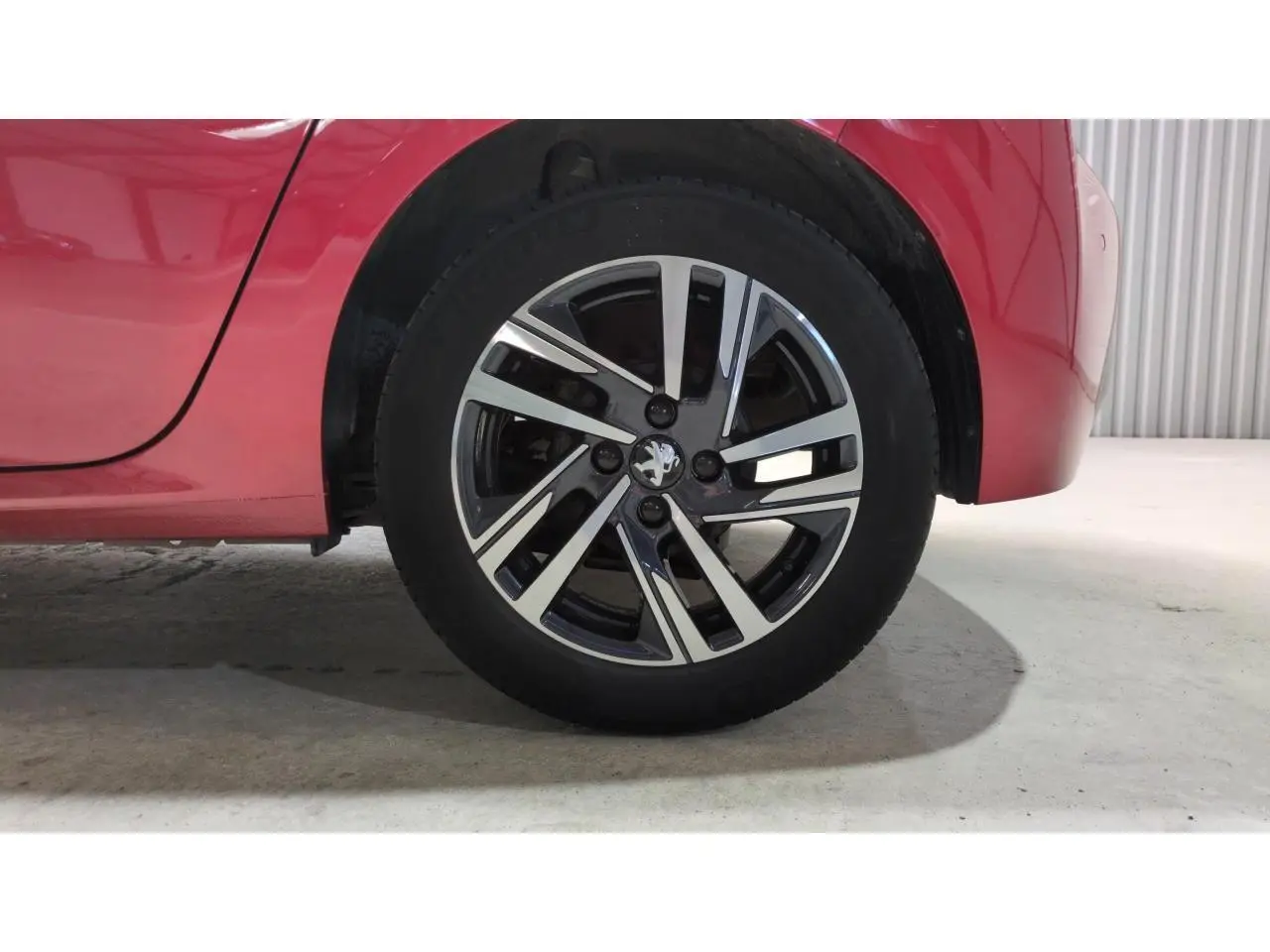 Gros plan sur la roue arrière droite d'une Peugeot 208 2024 rouge Elixir avec jante alliage bicolore.
