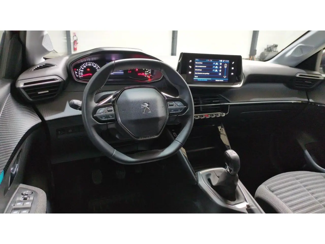 Vue intérieure avant du poste de conduite de la Peugeot 208 2024, avec volant compact et écran tactile central.