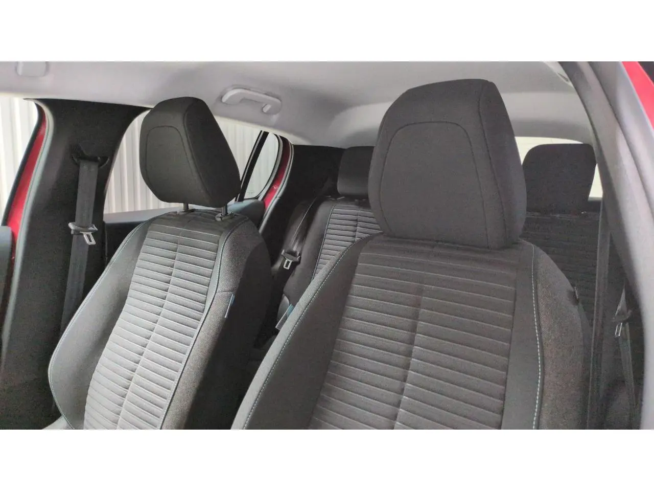 Vue intérieure des sièges avant et arrière noirs de la Peugeot 208 2024 Rouge Elixir, côté conducteur ouvert.