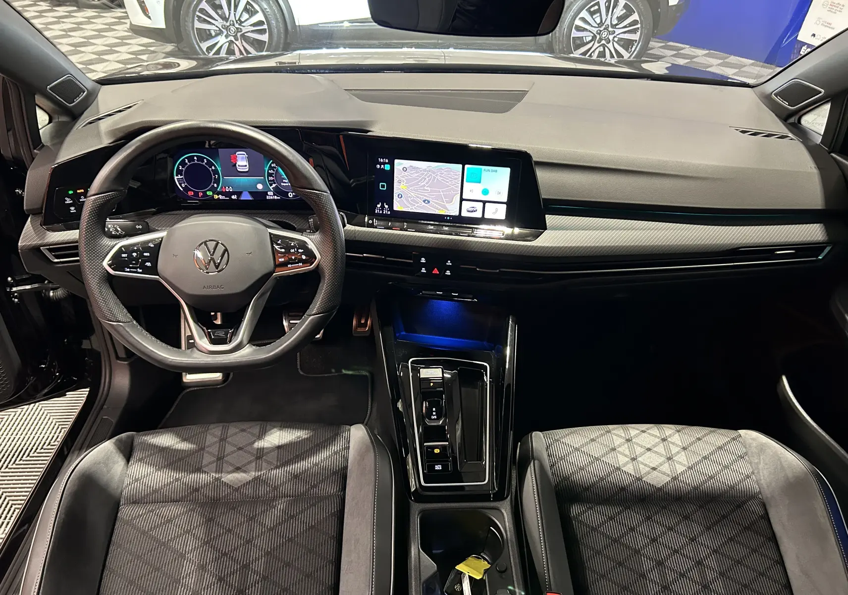 Vue intérieure avant de la Volkswagen Golf VIII eTSI noire, avec tableau de bord numérique et écran tactile central.