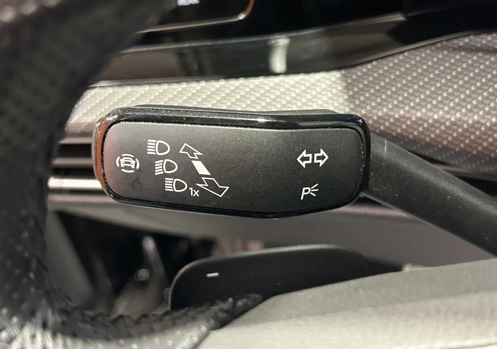 Gros plan sur la commande de clignotants noire à gauche du volant dans l’habitacle d’une Volkswagen Golf VIII noire.