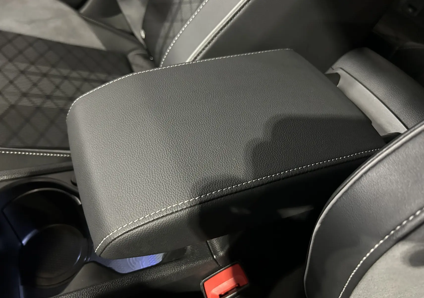 Gros plan sur l'accoudoir central en cuir noir avec surpiqûres blanches, intérieur de la Volkswagen Golf VIII eTSI 2024.