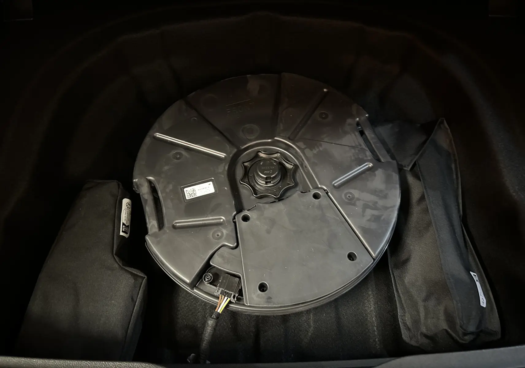 Vue rapprochée du coffre d’une Volkswagen Golf VIII eTSI 150CH R-Line noir métal, montrant la roue de secours et les accessoires de rangement.