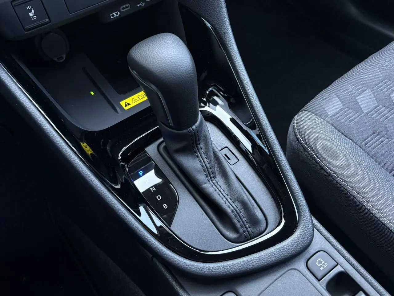 Le levier de vitesse automatique noir brillant de la Toyota Yaris hybride 2025 vu de dessus avec siège tissu gris à droite.