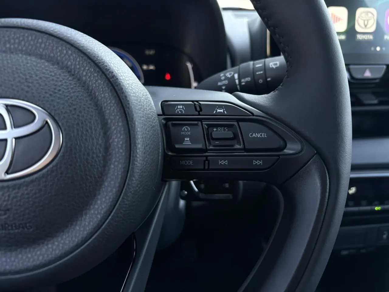 Gros plan sur le volant cuir noir de la Toyota Yaris 2025 hybride, avec commandes intégrées côté droit.