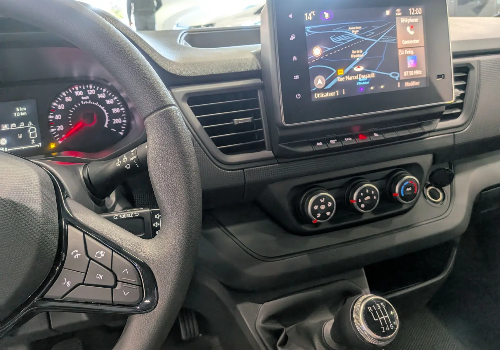 Vue intérieure du tableau de bord du Renault Trafic Combi 2025 gris, avec volant, écran tactile et levier de vitesses manuel.