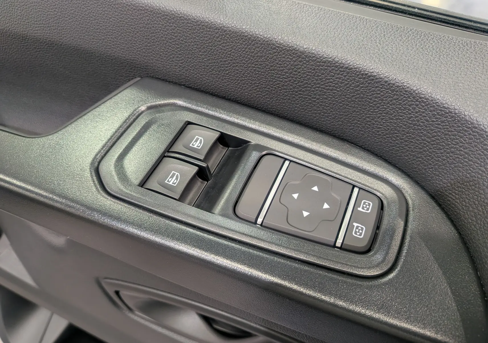 Gros plan sur les commandes de lève-vitres et réglage des rétroviseurs côté conducteur du Renault Trafic Combi gris.