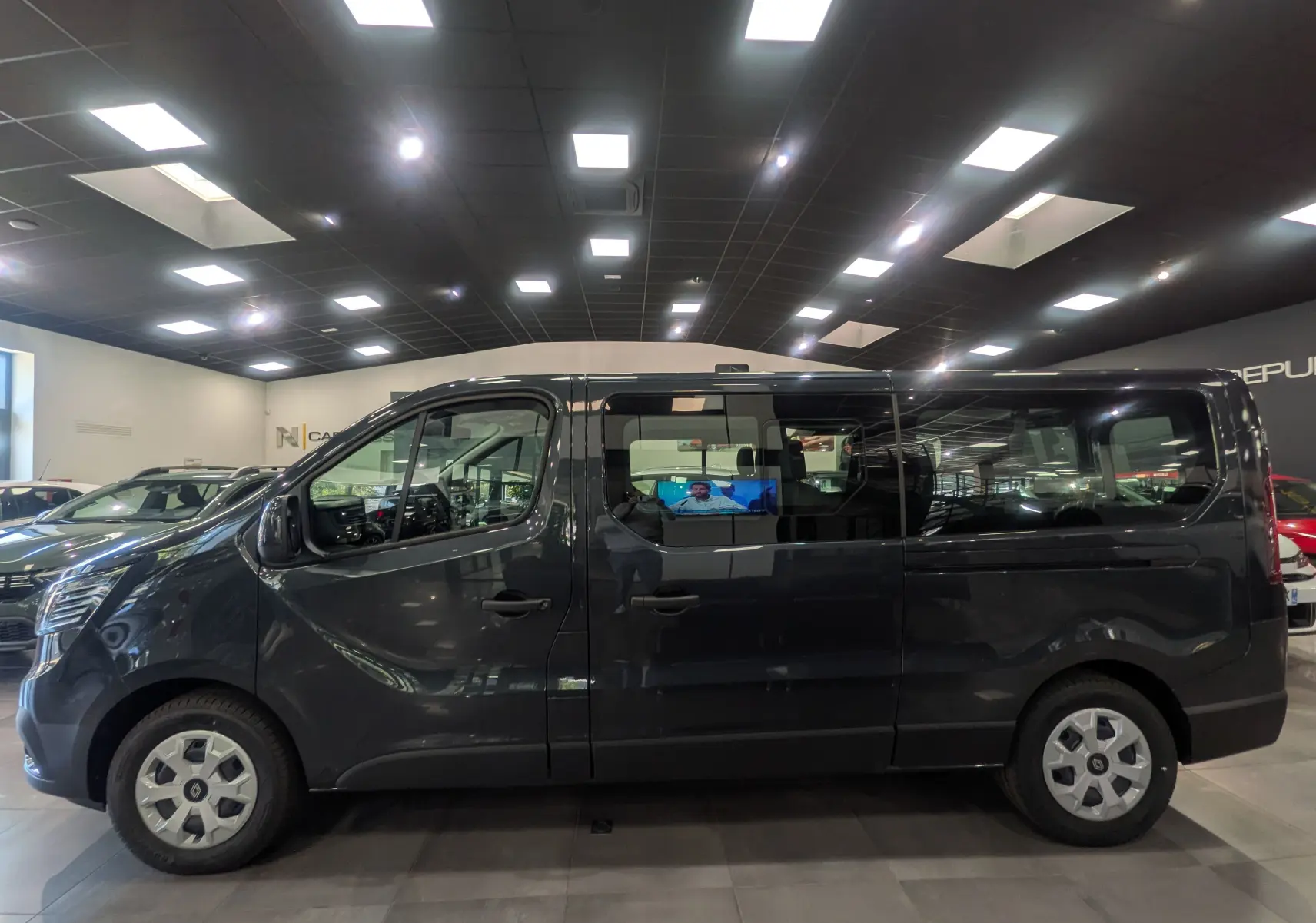 Vue latérale droite d'un Renault Trafic Combi gris Comète 2025 en showroom, avec vitres teintées et jantes acier.
