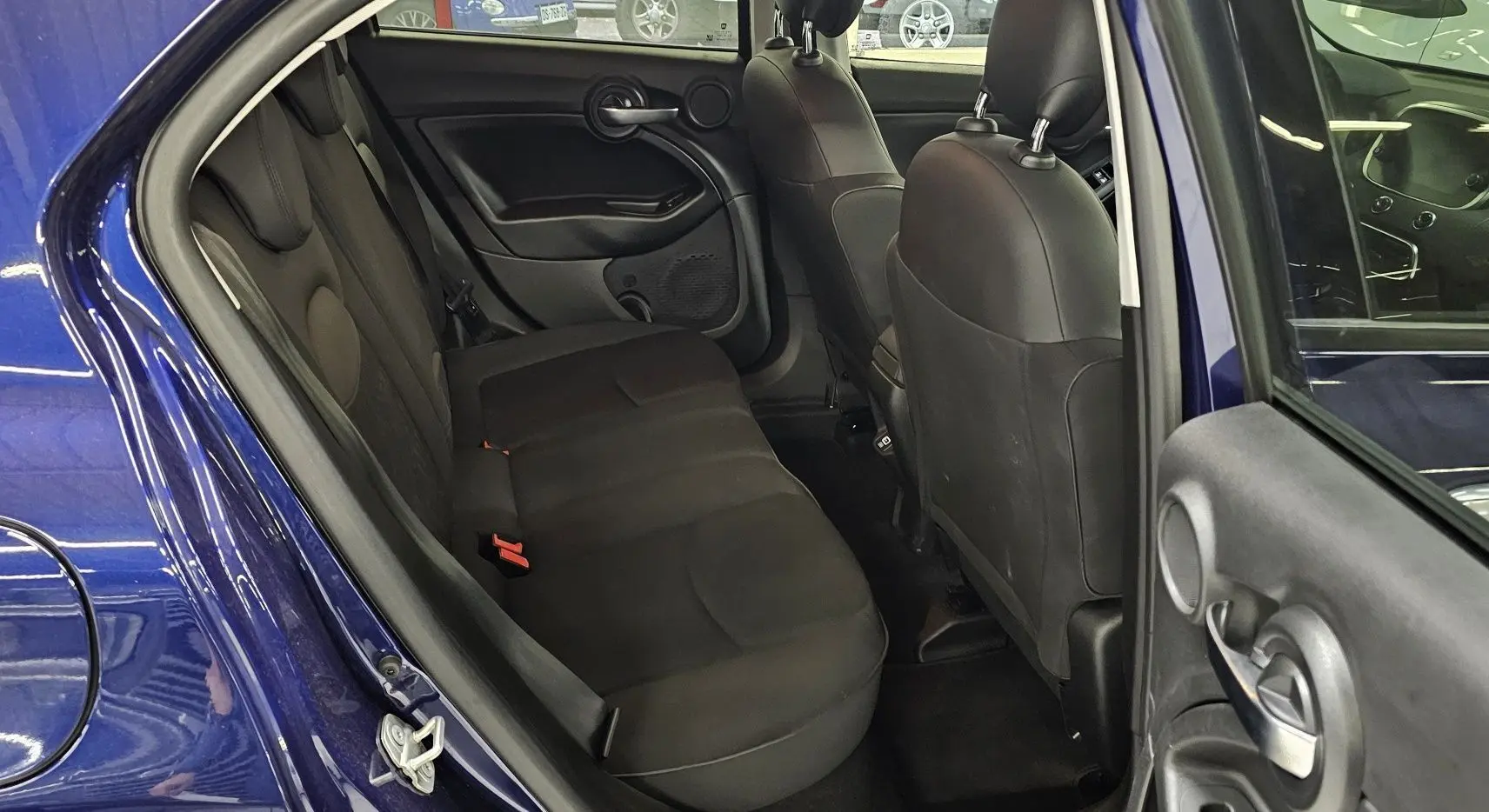 Vue intérieure arrière côté gauche d'une FIAT 500X 2024 bleue, montrant les sièges arrière noirs et la portière ouverte.