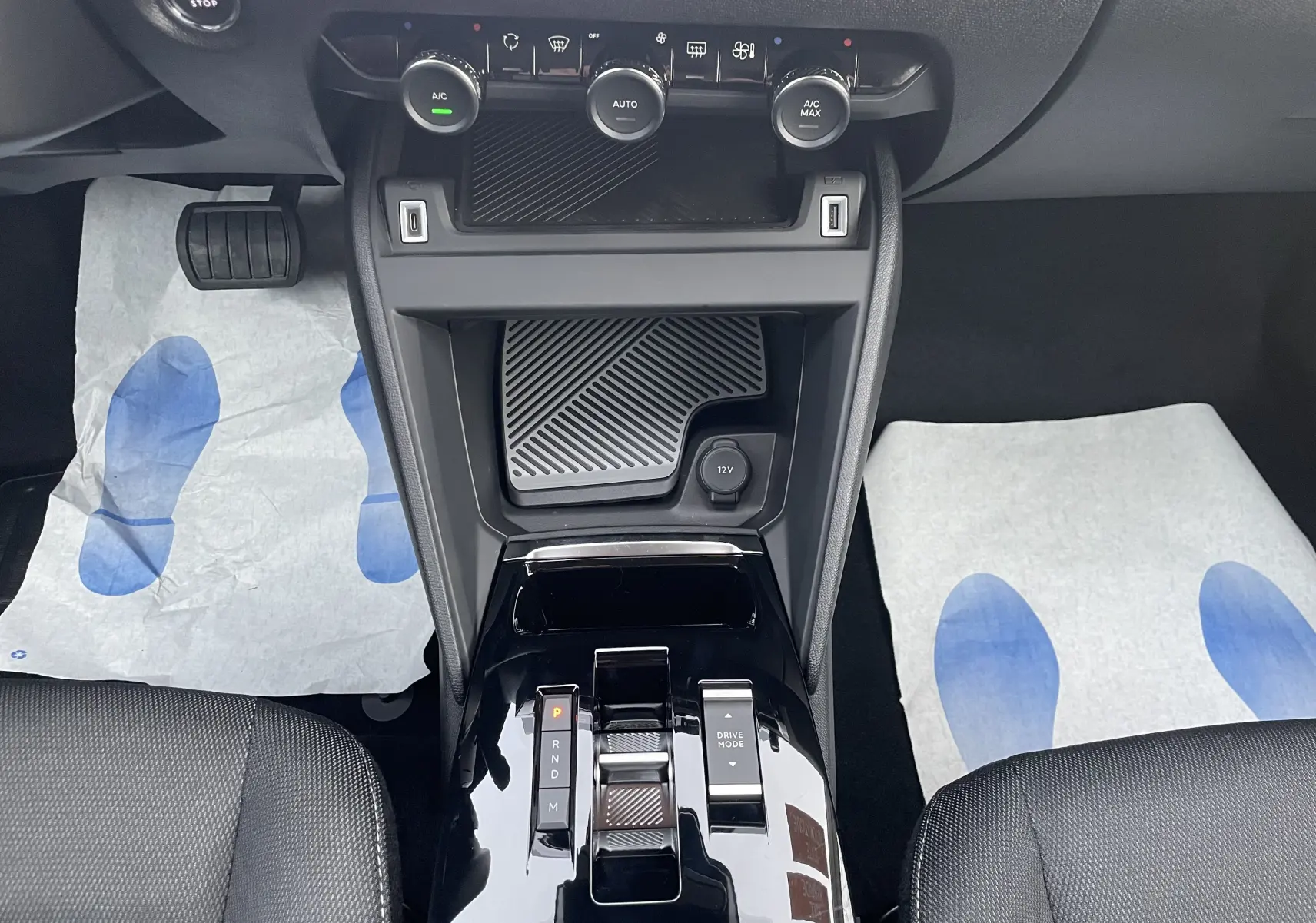 Vue intérieure centrée sur la console centrale noire brillante de la Citroën C4 hybride 2025 avec commandes climatisation et boîte auto.